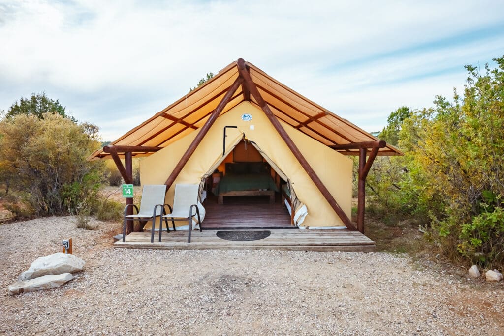 A spacious glamping tent with a wooden deck and chairs, surrounded by greenery.